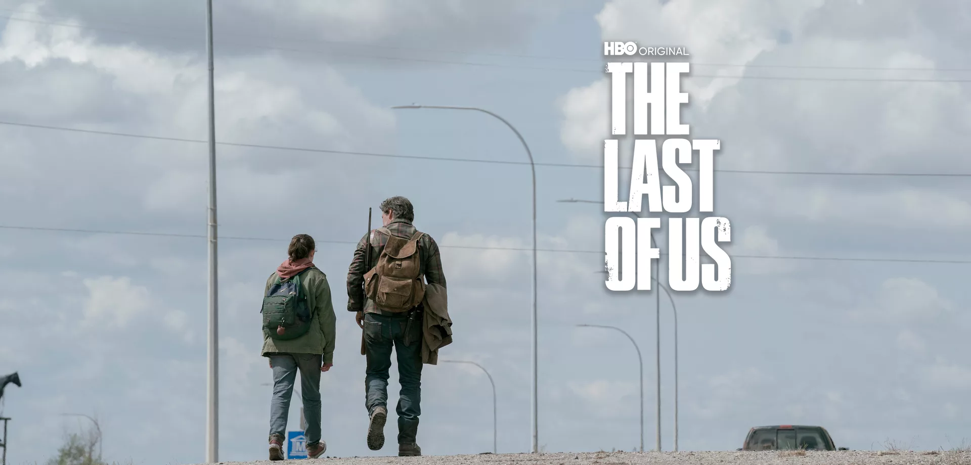 Ellie e Joel interpretados por Bella Ramsey e Pedro Pascal caminham em uma rodovia abandonada durante o dia e a logo de The Last of Us ao lado direito.