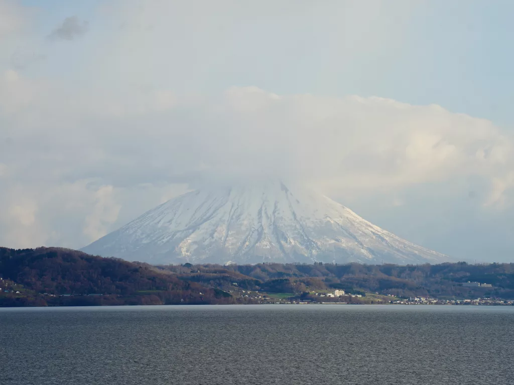 Foto do Monte Yōtei, da pequena cidade à frente e de águas.