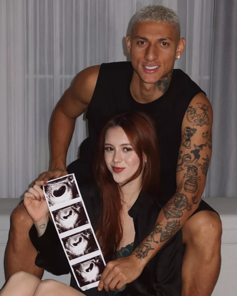 Richarlison e Amanda sentados no sofá com foto de futuro filho.