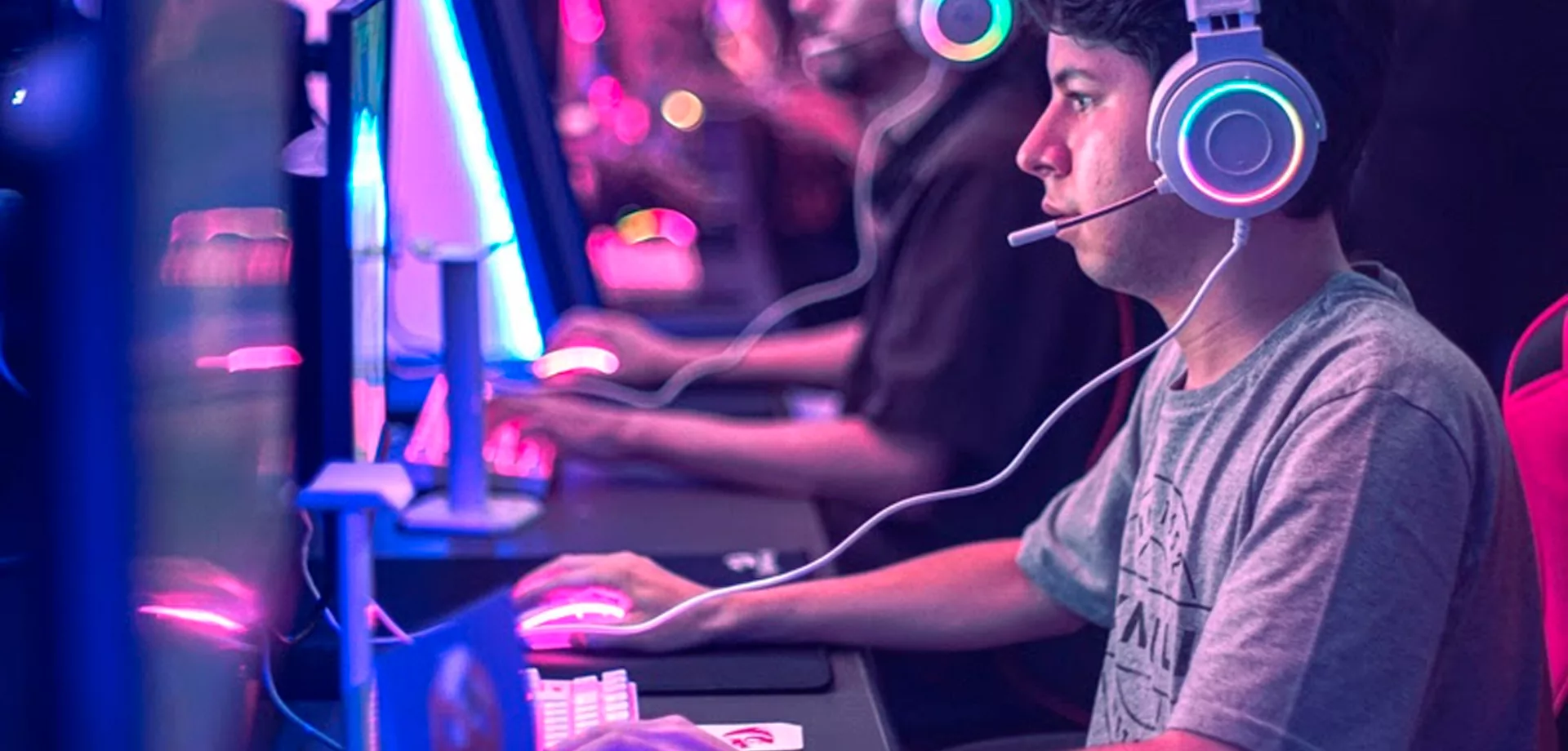 Pessoas jogando em PCs com luzes entre o azul e o rosa na Arena Xdome.