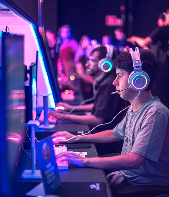 Pessoas jogando em PCs com luzes entre o azul e o rosa na Arena Xdome.