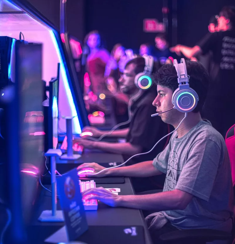 Pessoas jogando em PCs com luzes entre o azul e o rosa na Arena Xdome.