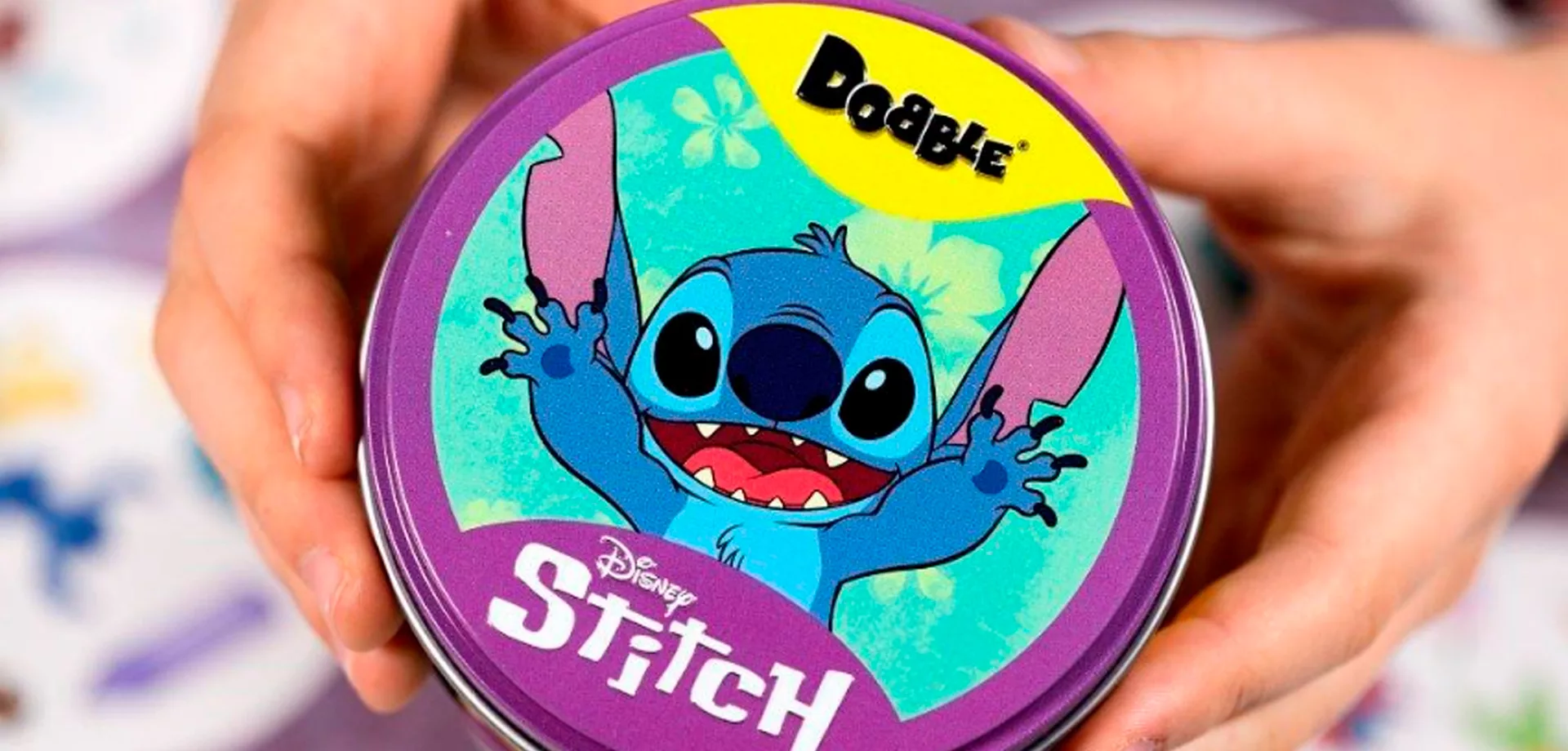 Mãos apresentam uma caixa circular metálica com a versão Dobble Stitch da Galápagos e Disney.