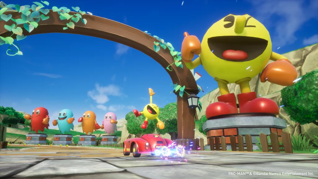 Pac-Man ao lado de sua estátua e em frente a estátua dos fantasmas e no seu carro vermelho.