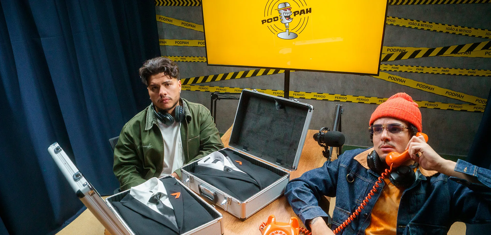 Mítico e Igão do PodPah sentados à mesa com um telefone laranja e dois ternos do The Replacer de Call of Duty Black Ops 7.