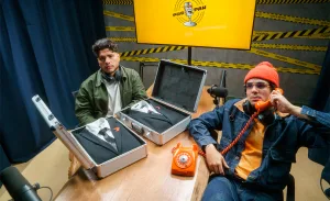 Mítico e Igão do PodPah sentados à mesa com um telefone laranja e dois ternos do The Replacer de Call of Duty Black Ops 7.