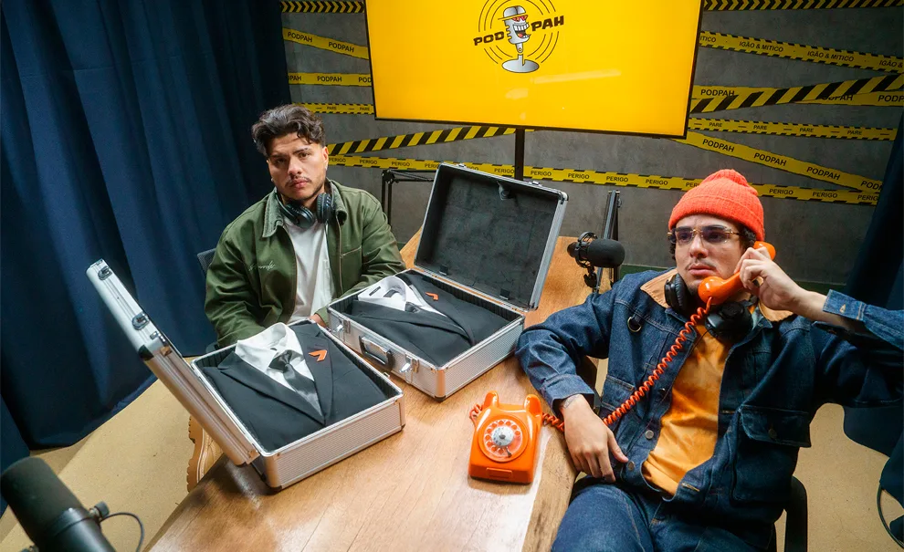 Mítico e Igão do PodPah sentados à mesa com um telefone laranja e dois ternos do The Replacer de Call of Duty Black Ops 7.