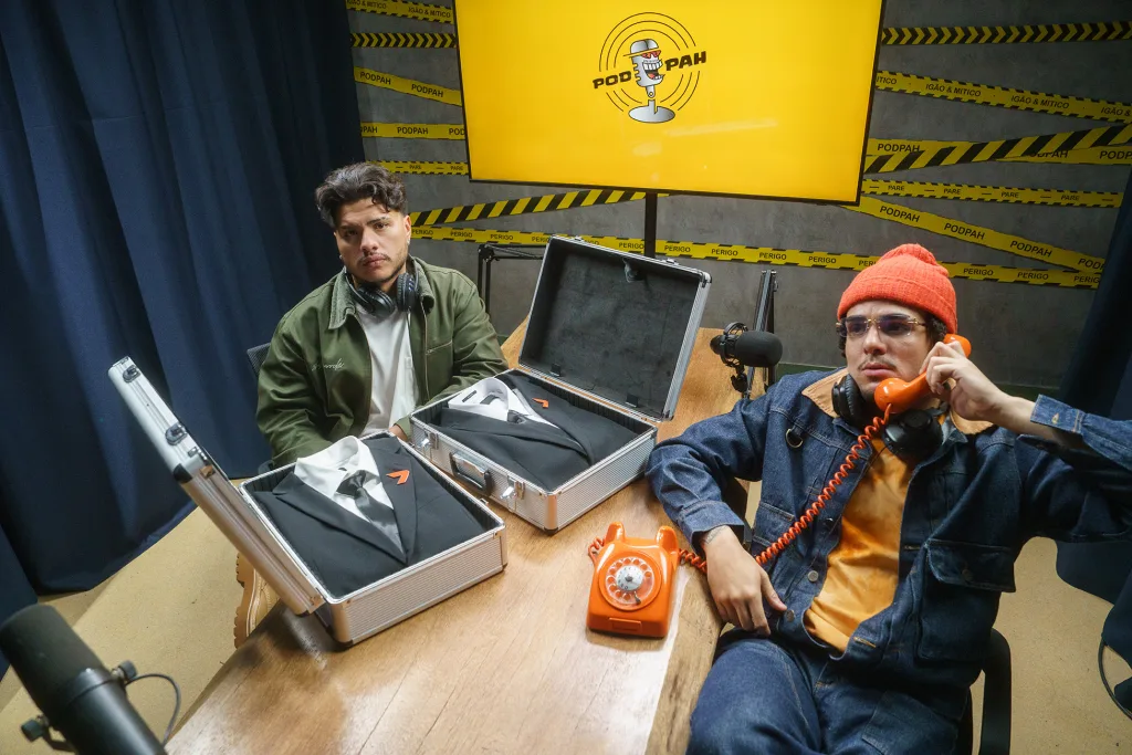 Mítico e Igão do PodPah sentados à mesa com um telefone laranja e dois ternos do The Replacer de Call of Duty Black Ops 7.