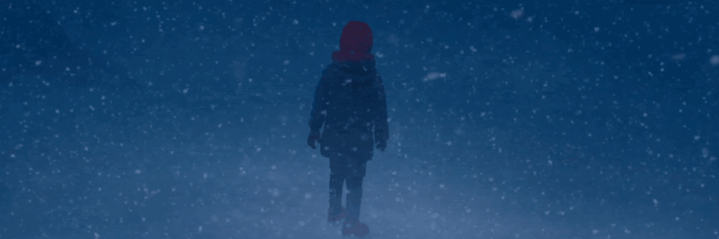 Criança com roupa de frio e de costas para a imagem, ela está na neve.