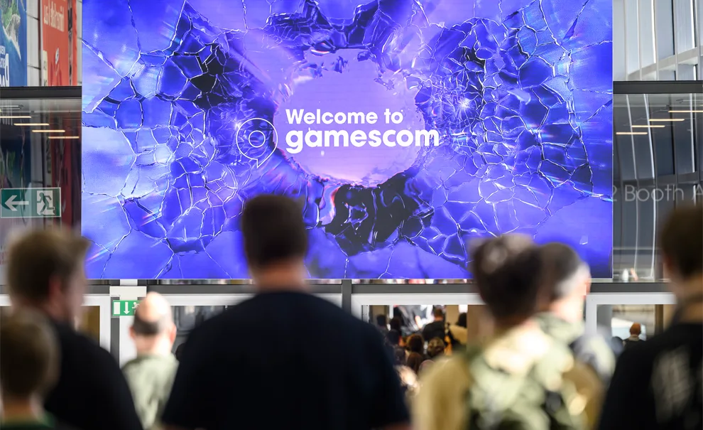 Foto da gamescom 2026 com pessoas à frente de um telão escrito "Welcome to gamescom".