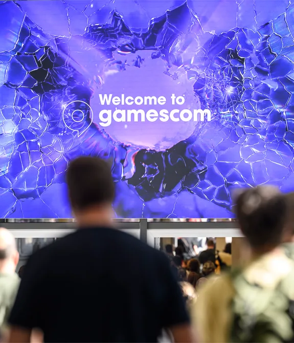 Foto da gamescom 2026 com pessoas à frente de um telão escrito "Welcome to gamescom".